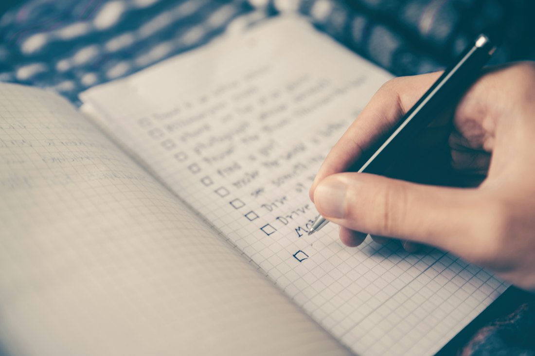A checklist written on paper beside a laptop and a cup of coffee